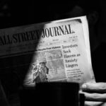 A monochrome photograph capturing a person reading The Wall Street Journal.